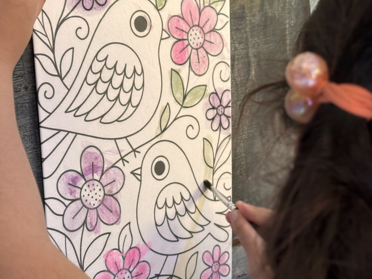 Manos coloreando un dibujo de un ave con flores