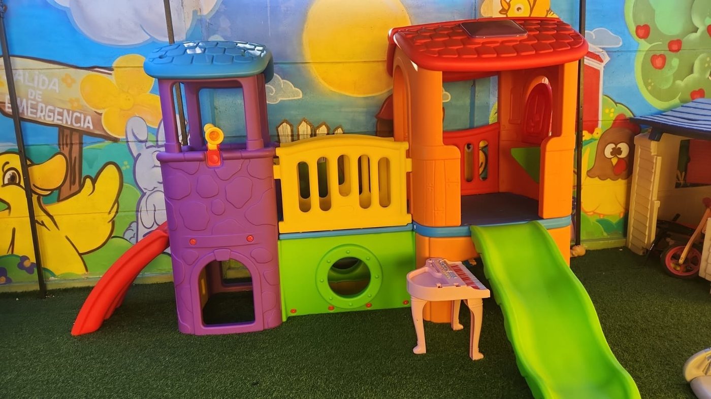 Casita de juegos con resbalín y mobiliario infantil en el patio