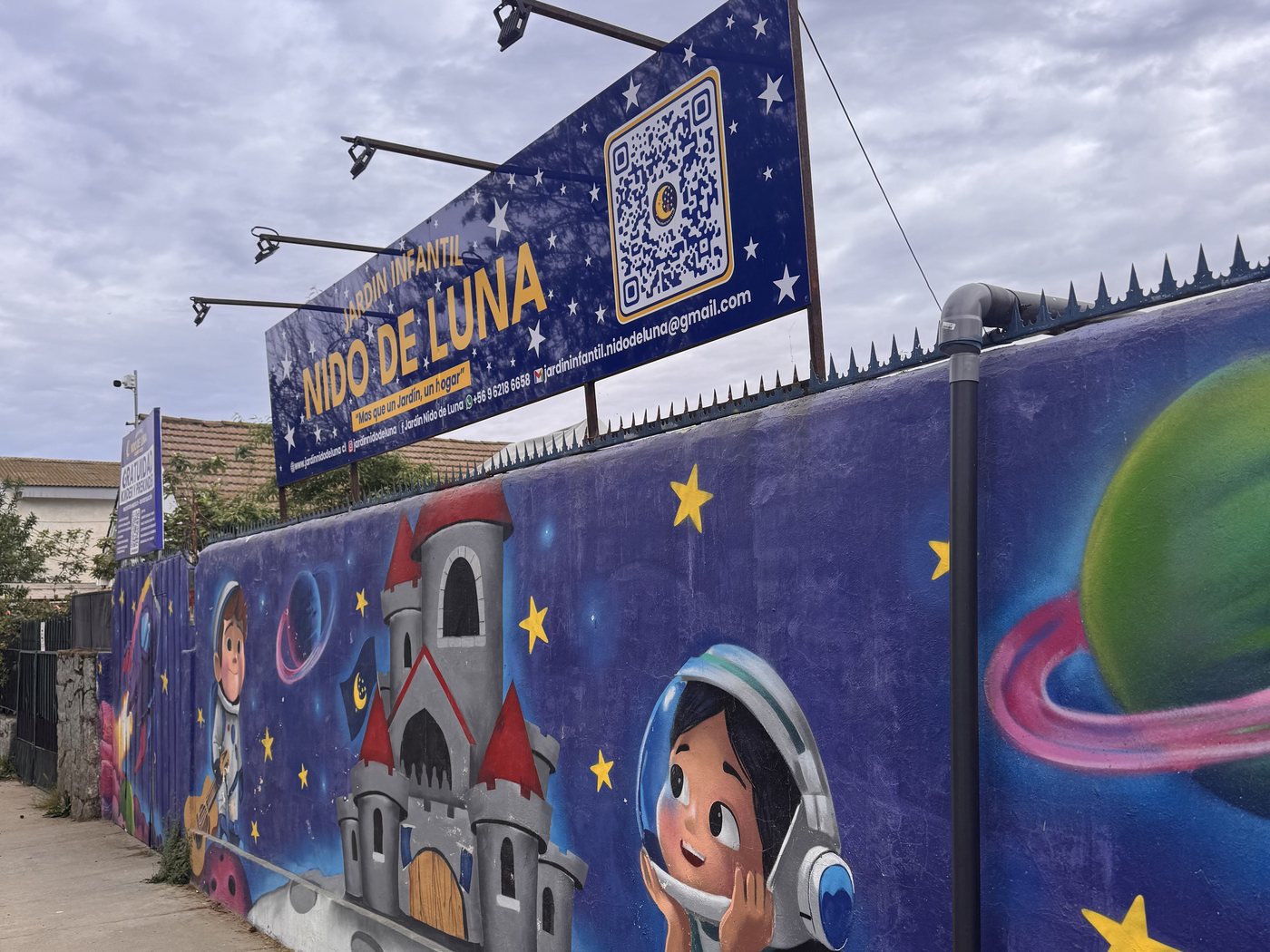 Muro lateral del jardín pintado con planetas y estrellas, bajo el letrero