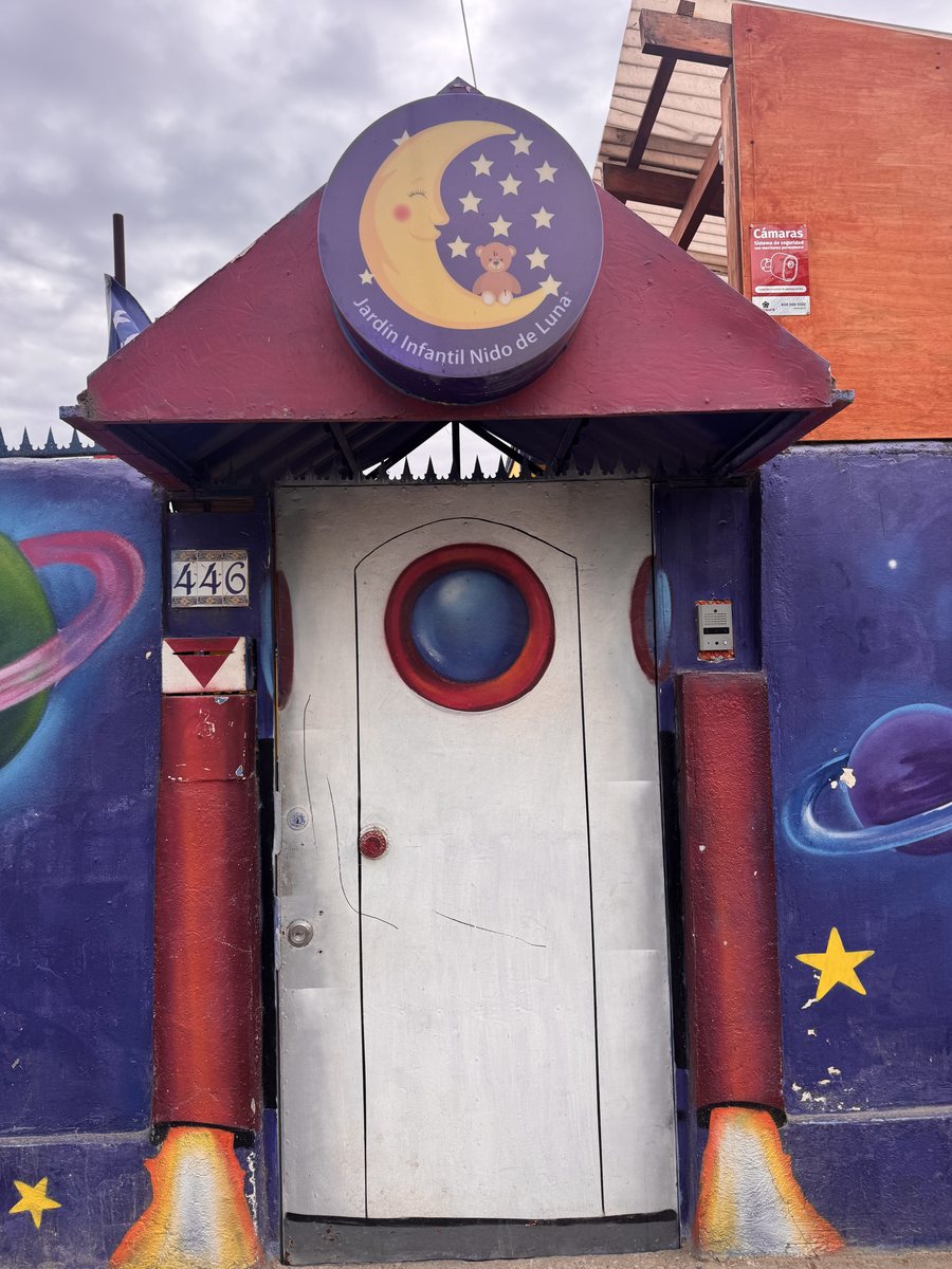 Puerta de entrada del jardín pintada como un cohete, con la luna y el osito del logo arriba