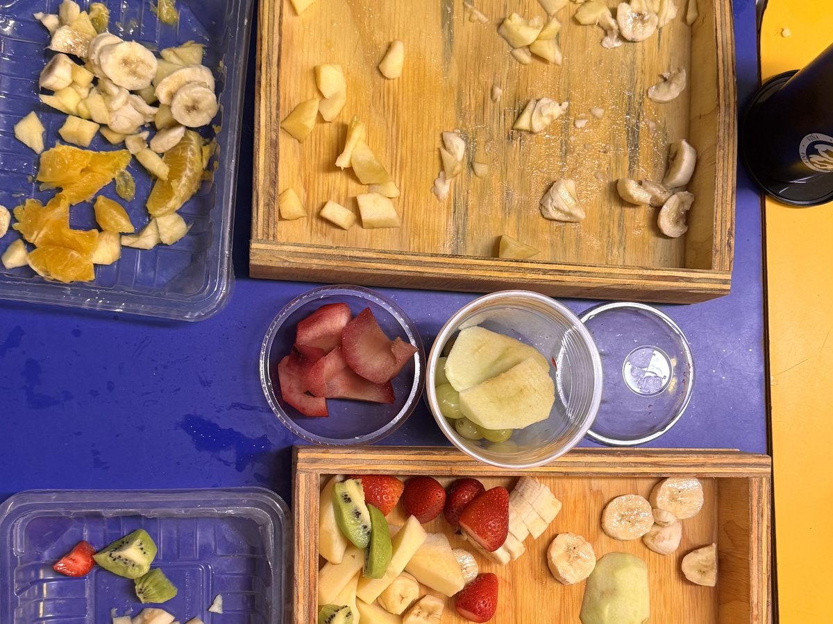 Manos de niños preparando fruta picada en una bandeja durante el taller de cocina